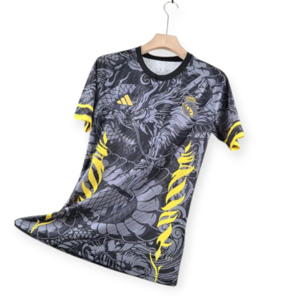 Real Madrid football jersey on a wooden hanger with a black collar and yellow accents, featuring the club crest and Adidas logo on a dark patterned fabric.