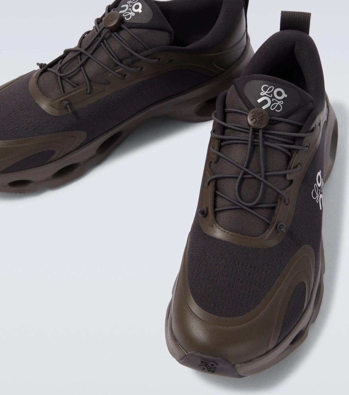 Close-up of a dark brown athletic shoe showing laces, eyelets, and logo on the tongue, pair at an angle.