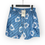 Blue shorts featuring a repeating Dior monogram pattern with white paint splatter details, displayed on a hanger with a tag attached