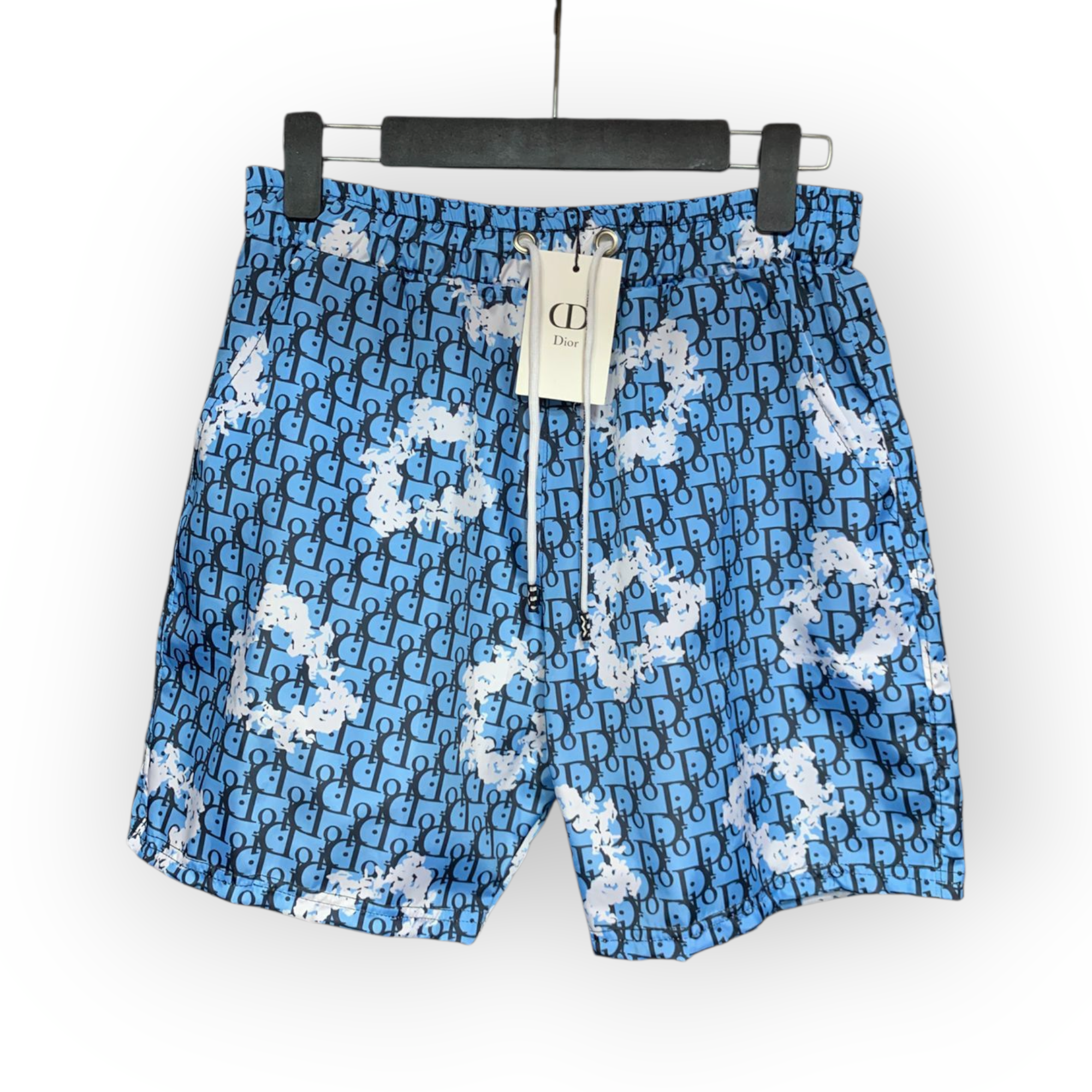rn-image_picker_lib_temp_b23be6eb-9e4a-4b9f-a073-bae947cc72d5 Blue shorts featuring a repeating Dior monogram pattern with white paint splatter details, displayed on a hanger with a tag attached