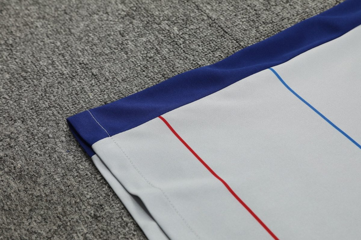Close-up of light gray fabric with blue edge and a red seam, lying on a gray carpet.