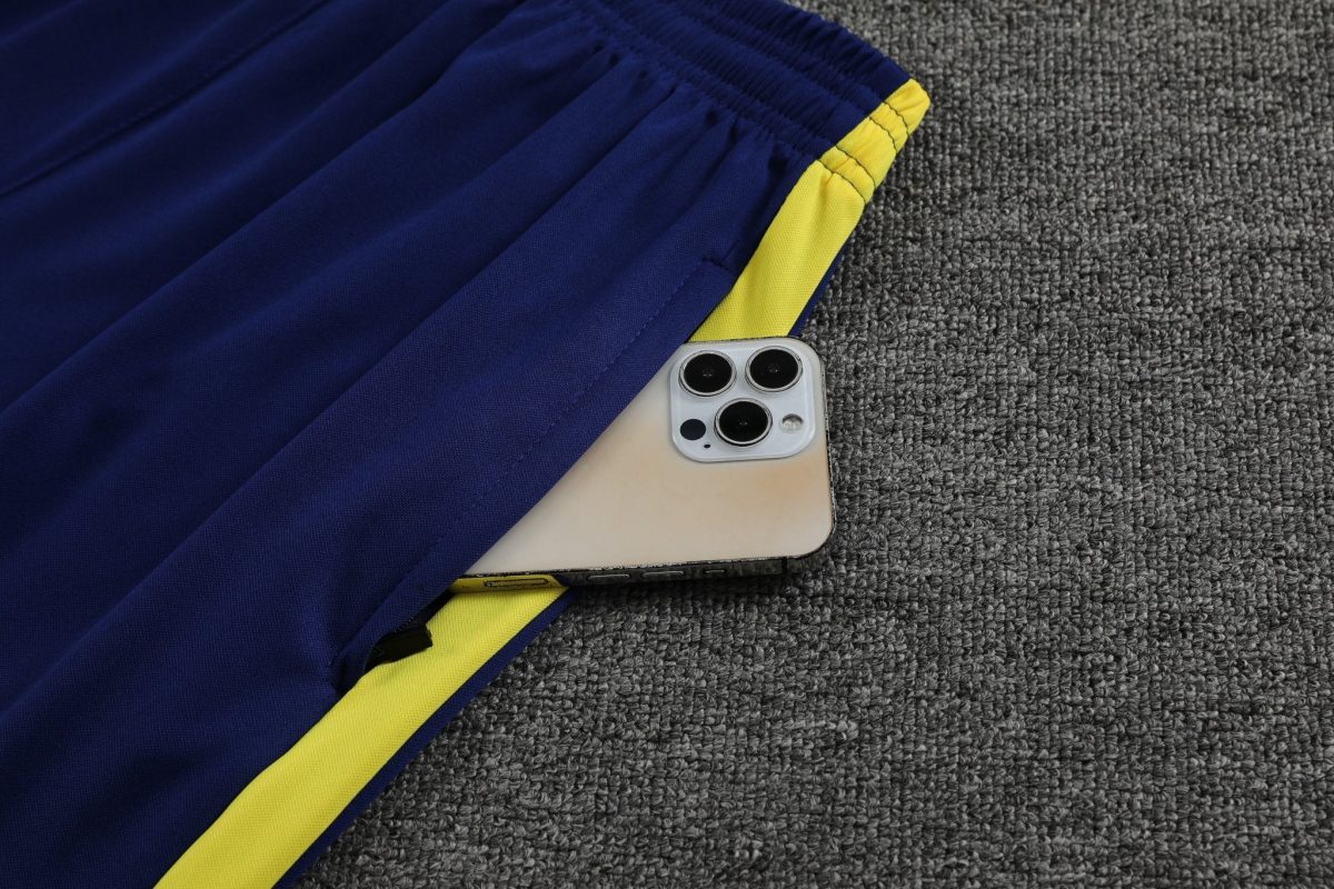 Close-up of a smartphone partially tucked under a blue and yellow gym jacket on a gray carpeted floor, shot from above.