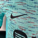 Close-up of turquoise fabric with red and blue stitch patterns and a partial black Nike swoosh logo photographed on the material surface.