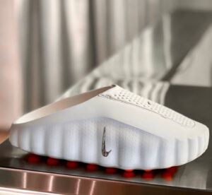 White Nike sneaker with perforated upper and silver swoosh, resting on a metal surface.
