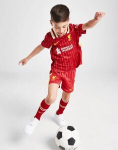 rn-image_picker_lib_temp_c0d624b1-d74f-49df-8196-b53c4564f171 | UAE SPORT STORE Young child in a red soccer kit kicks a black-and-white soccer ball on a white backdrop, mid-action stance.