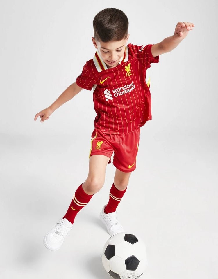 rn-image_picker_lib_temp_c0d624b1-d74f-49df-8196-b53c4564f171 | UAE SPORT STORE Young child in a red soccer kit kicks a black-and-white soccer ball on a white backdrop, mid-action stance.