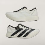 White athletic sneaker with black three-stripe design and signature on the heel, featuring a chunky sole and light-gray upper details.