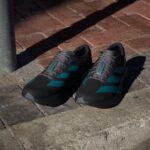Pair of gray and teal running shoes resting on a brick sidewalk with shadows across the ground