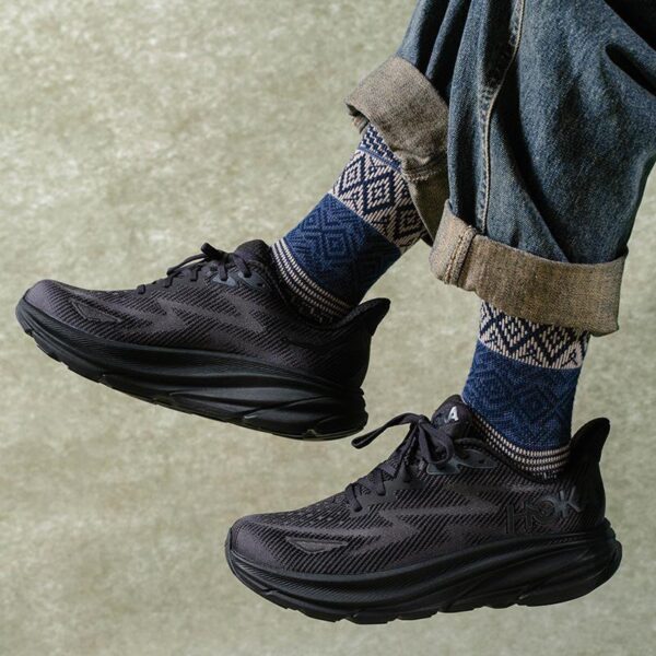 Black athletic sneakers with dark patterned socks and rolled denim cuffs against a concrete background.