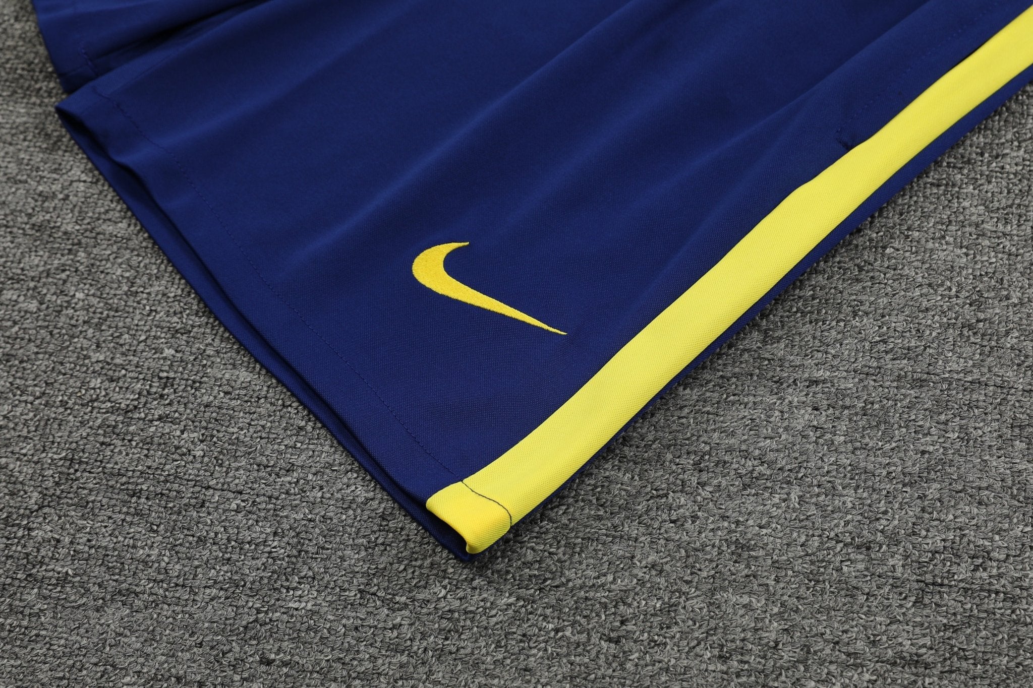 rn-image_picker_lib_temp_cd4e2e0f-517c-4f29-92e4-b6f4ecc1a677 | UAE SPORT STORE Blue athletic pants with a yellow stripe and Nike swoosh on a gray carpeted surface in the background.