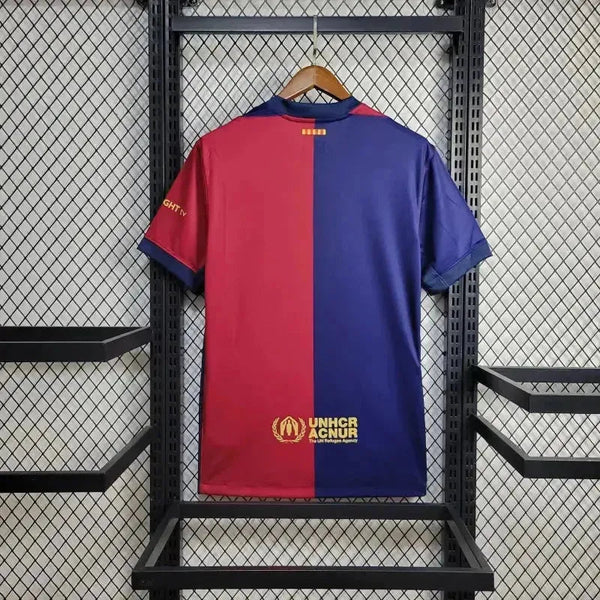 Back view of a red-and-blue split jersey hanging on a hanger in a metal rack; UNHCR logo at the bottom.