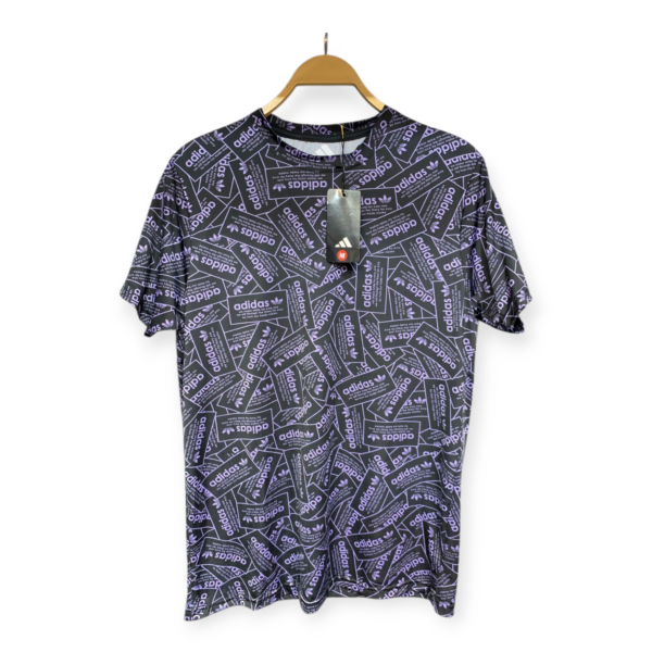 Shirt on a wooden hanger with a purple adidas allover patent-text pattern and a black tag attached in front, viewed from the chest area.