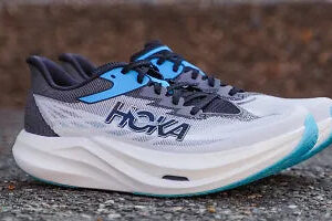 Side view of a blue and gray HOKA running shoe with a teal sole on a pavement surface.
