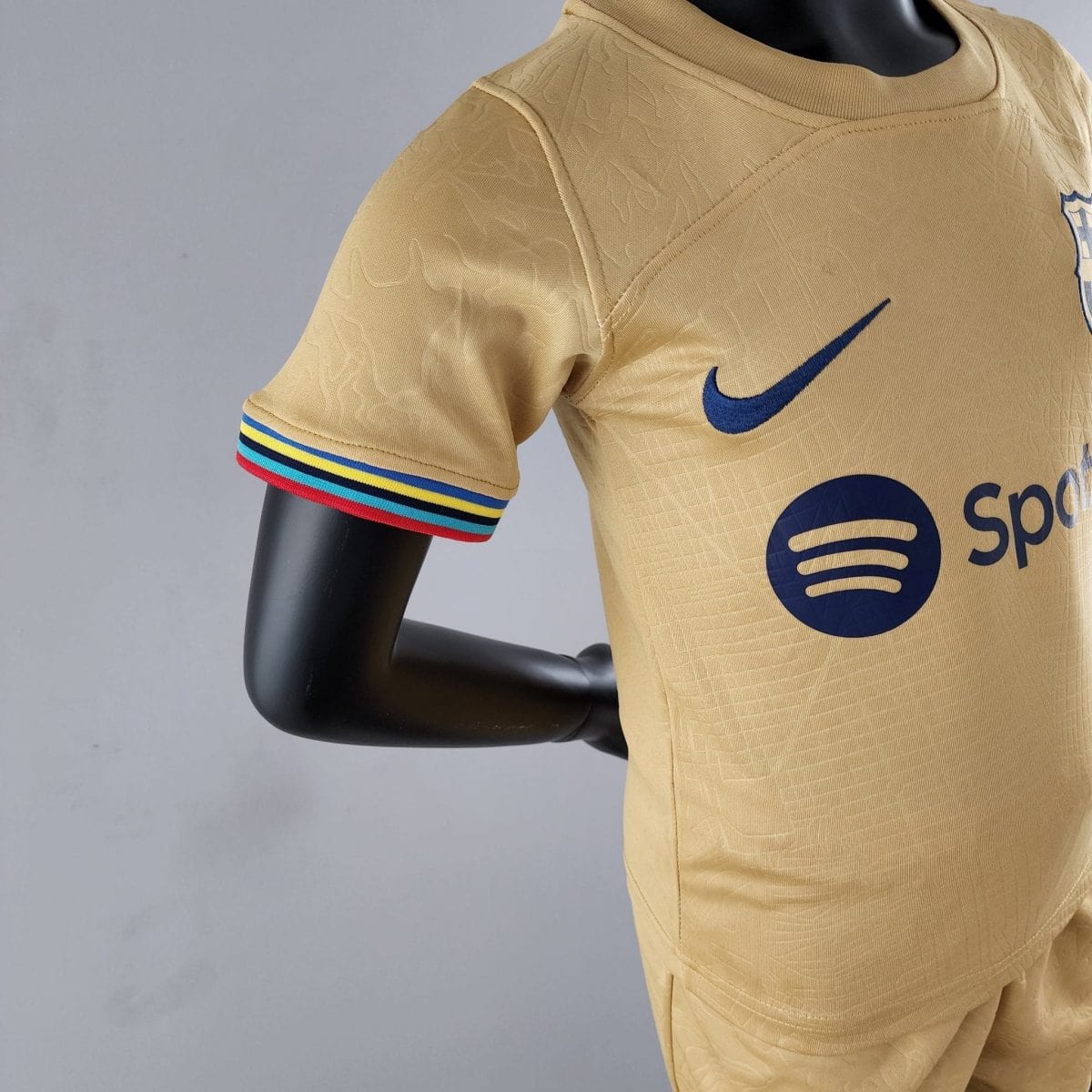 Close-up of a beige athletic jersey sleeve with a blue Nike swoosh and a striped cuff on a mannequin arm.
