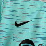 Close-up of turquoise fabric with red and blue stitch marks and a partial black Nike swoosh logo.