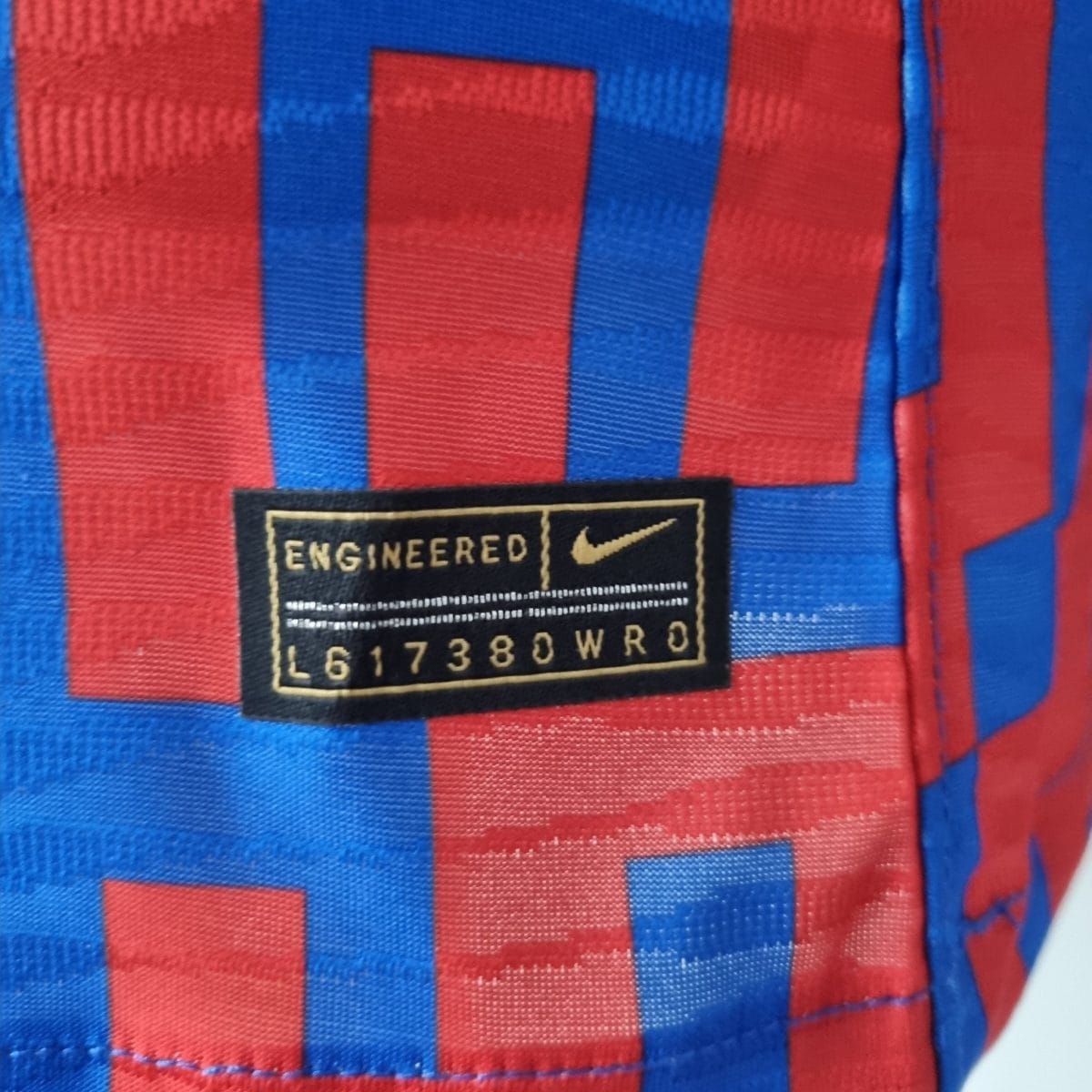 Close-up of red and blue striped fabric with a black label that reads ENGINEERED and includes a swoosh logo.