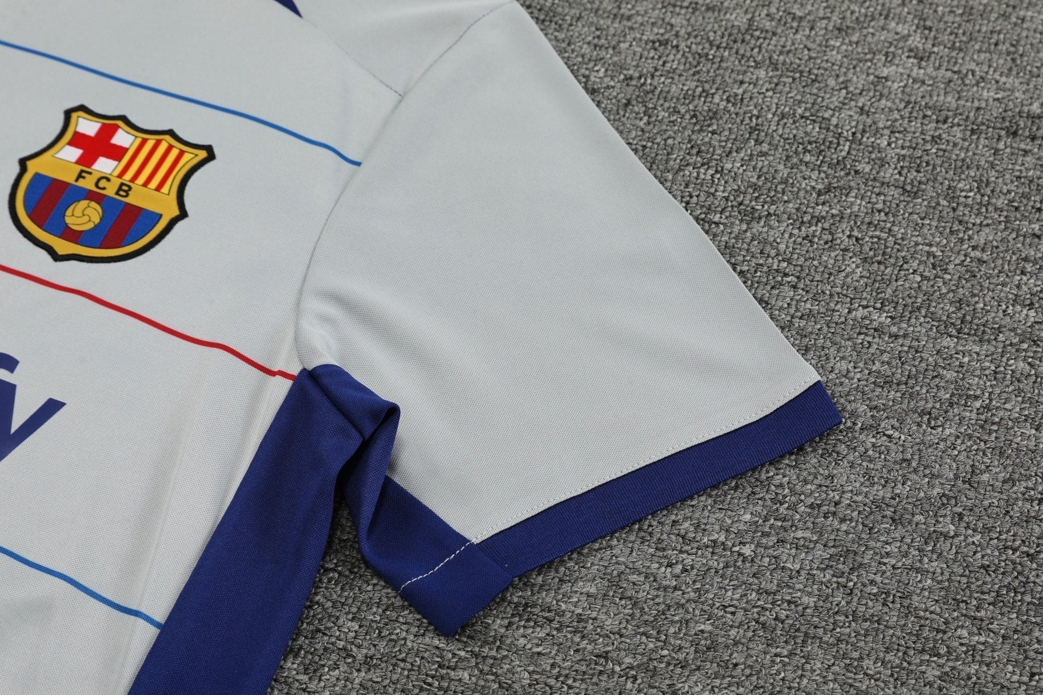 rn-image_picker_lib_temp_dea02027-bb6f-402a-9323-79fe60bfc092 | UAE SPORT STORE Partially folded white FC Barcelona football jersey on a gray carpet, showing the club crest and blue trim.