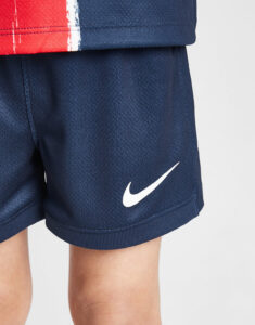 Navy blue athletic shorts with a white Nike swoosh logo near the hem on the leg of a child or person wearing red and blue clothing above.