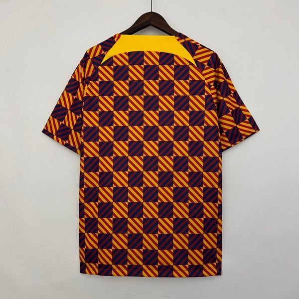 Shirt on a hanger with a bold yellow collar and a repeating navy-and-yellow diagonal checker pattern on red background.