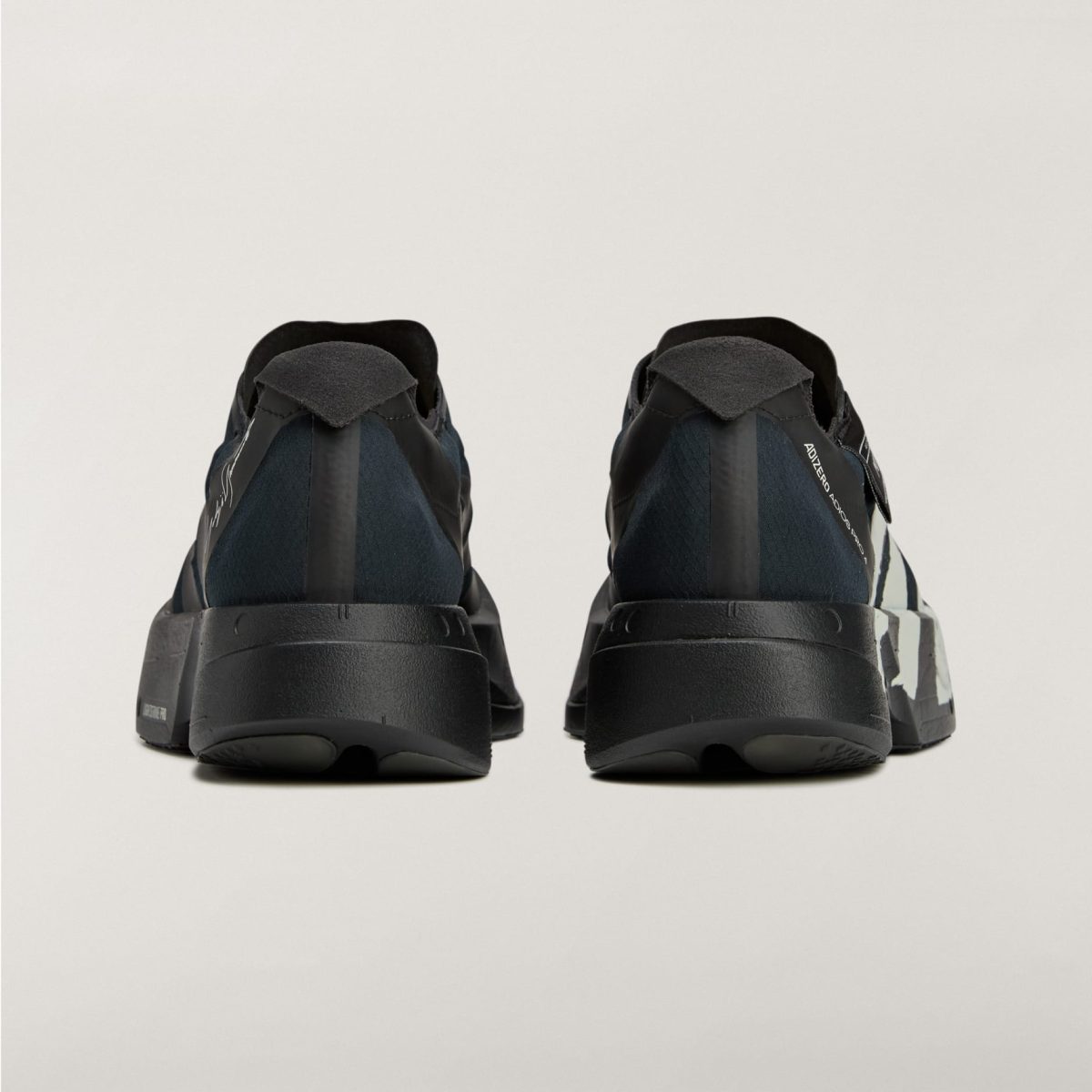 Rear view of two black athletic sneakers standing side by side on a light background with visible heel straps and soles.