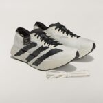 Pair of white and black sneakers with black laces on a pale background, with extra white laces nearby.