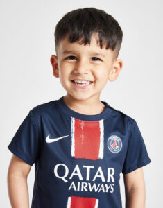 Smiling young boy wearing a navy PSG jersey with red stripes and the Qatar Airways logo, facing camera.