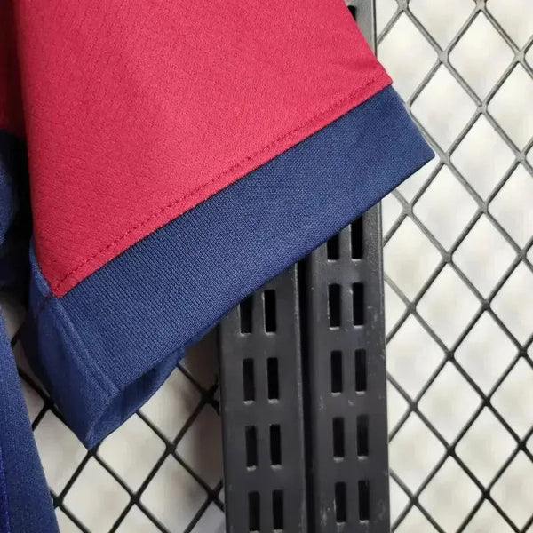 rn-image_picker_lib_temp_e39759a0-0679-41a7-bd6b-0f84bfe9813a | UAE SPORT STORE Close-up of red fabric with a blue edge draped over a black metal rack against a diamond-pattern fence background.