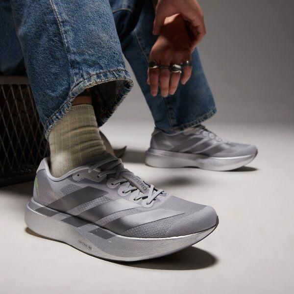 Gray athletic sneakers on a person wearing denim jeans and beige socks, feet resting on the floor in a studio setting