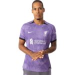 rn-image_picker_lib_temp_eb335c4a-ea34-46ed-bbf3-67d1e630970d | UAE SPORT STORE Man wearing a purple Liverpool FC jersey with Standard Chartered sponsor, facing front with hands clasped.