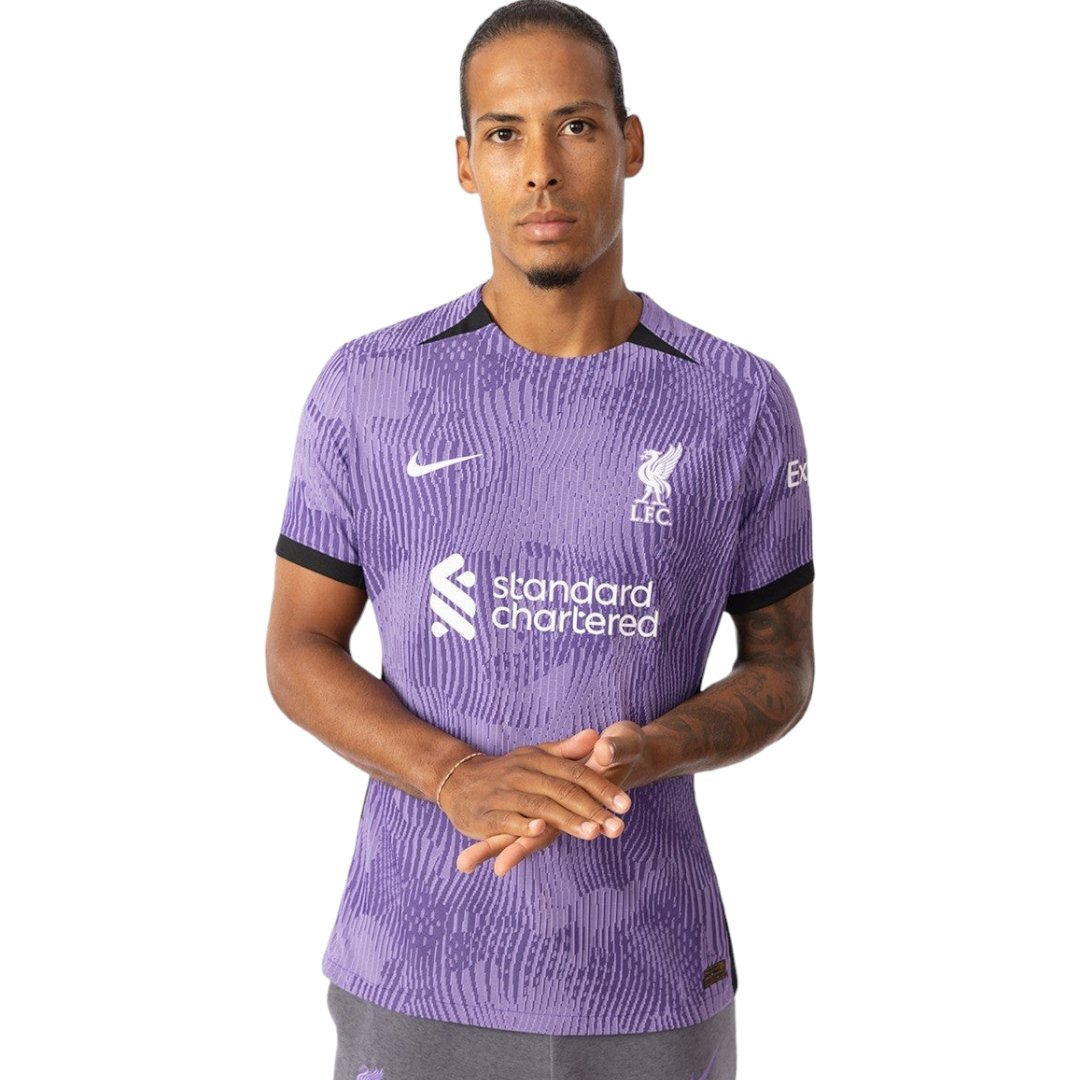rn-image_picker_lib_temp_eb335c4a-ea34-46ed-bbf3-67d1e630970d | UAE SPORT STORE Man wearing a purple Liverpool FC jersey with Standard Chartered sponsor, facing front with hands clasped.