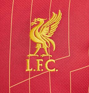 Gold embroidered Liverpool FC crest (bird with wings) above 'L.F.C.' on red fabric, likely a football jersey detail.