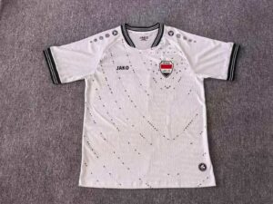 White soccer jersey laid flat with black trim, Iraq crest on chest, JAKO logo, and dotted pattern across the fabric.