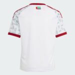 Back view of a white polo with red collar and sleeve trim; a small UAE flag sits at the neckline center.