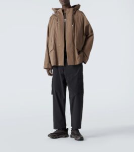 Full-body view of a person wearing a brown hooded jacket, black cargo pants, and brown sneakers, standing against a light background.