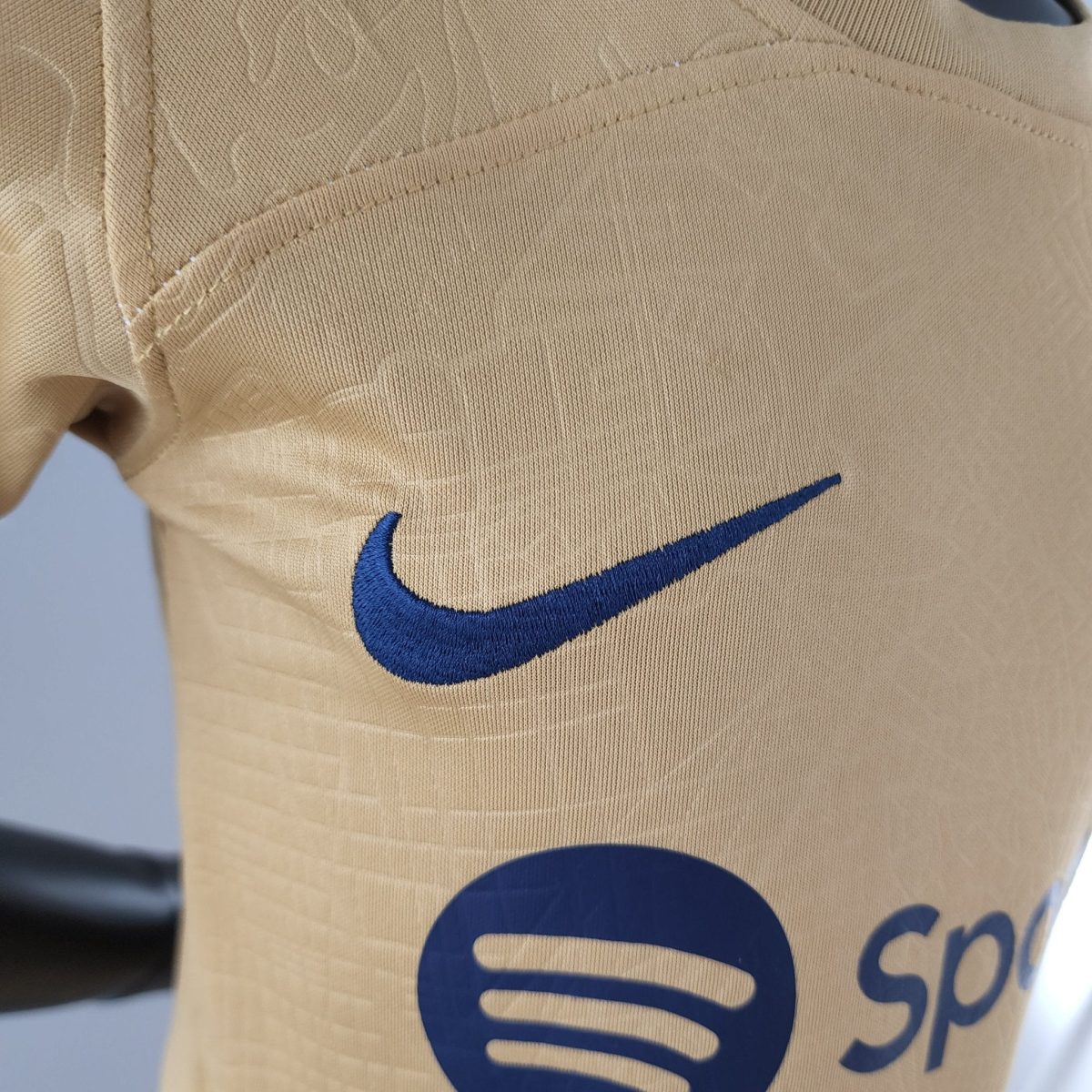 Close-up of beige fabric showing a blue Nike swoosh logo partially visible and stitching detail.