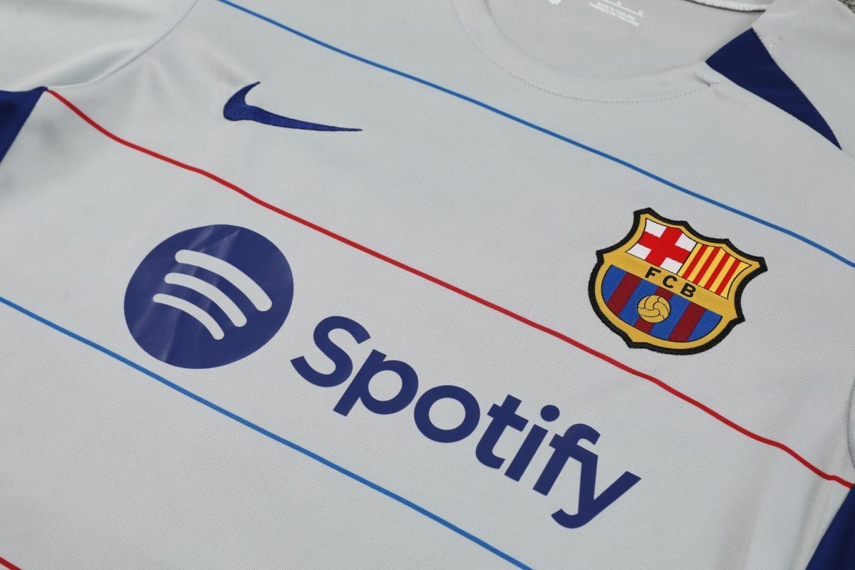 Close-up of a light gray Barcelona football jersey showing the FC Barcelona crest, a blue Nike swoosh, and sponsor logos.