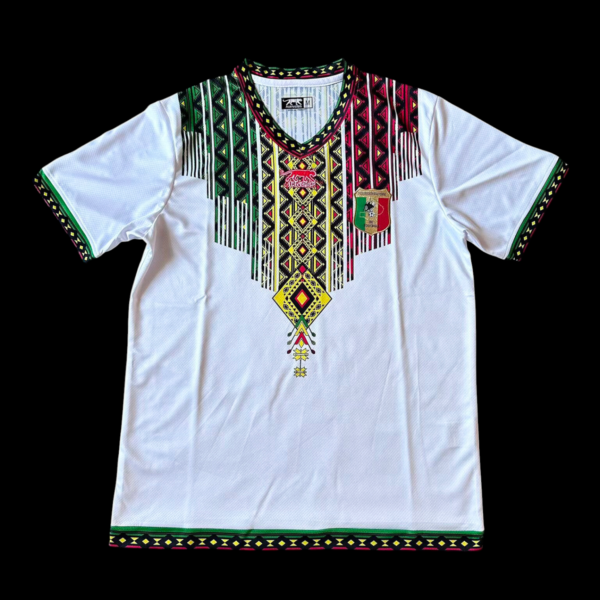 White short-sleeve dashiki with a multicolored geometric pattern around the neckline and fringe tassels; green trim on sleeves and hem.