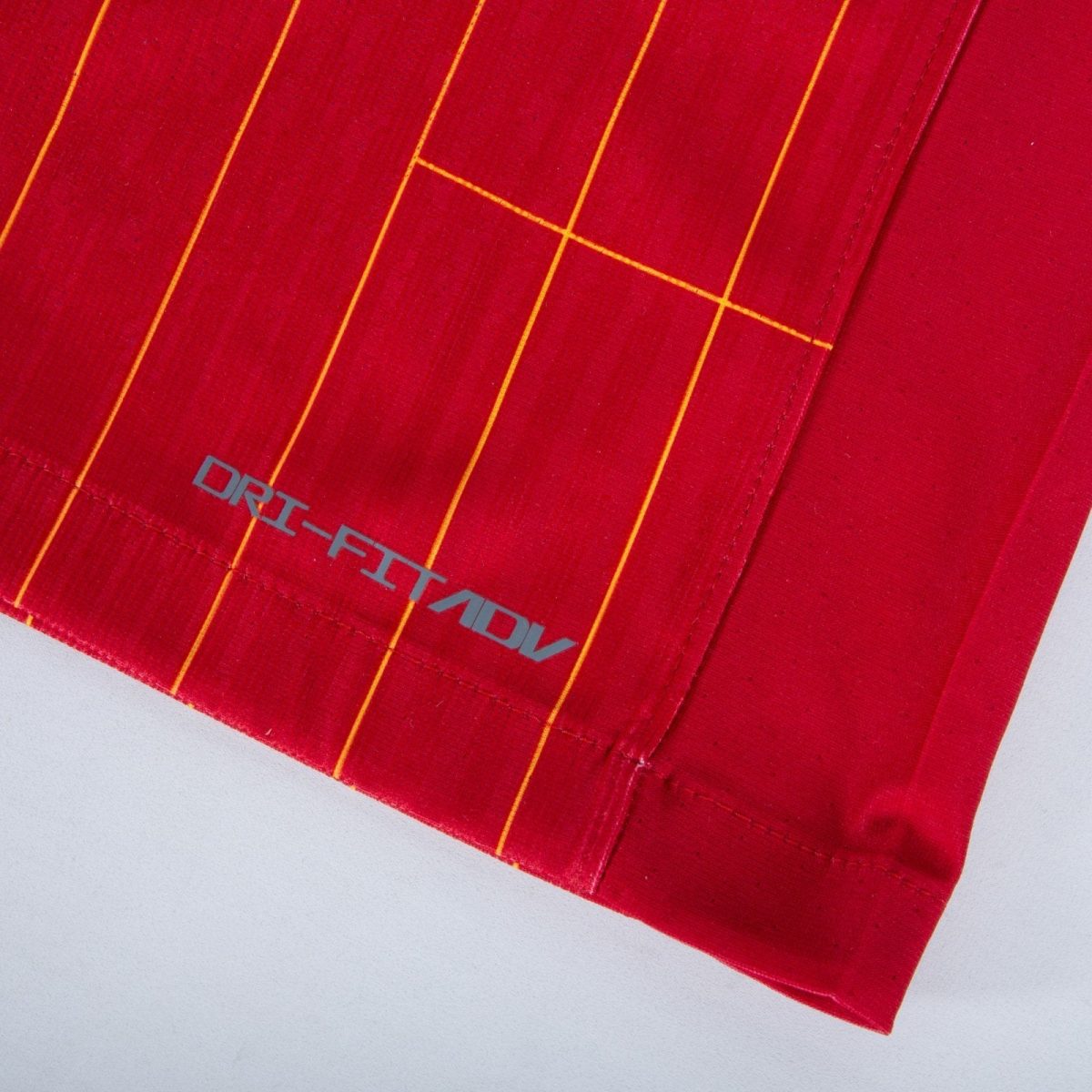 Close-up of red fabric with thin yellow-orange vertical stripes and a partial gray logo reading 'DRIFT' along the edge.