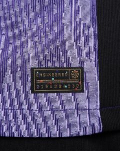 rn-image_picker_lib_temp_fbf162d4-6989-4f18-b32b-e8b98e2b1b23 | UAE SPORT STORE Close-up of purple patterned fabric with a small black tag reading ENGINEERED and a row of numbers nearby.