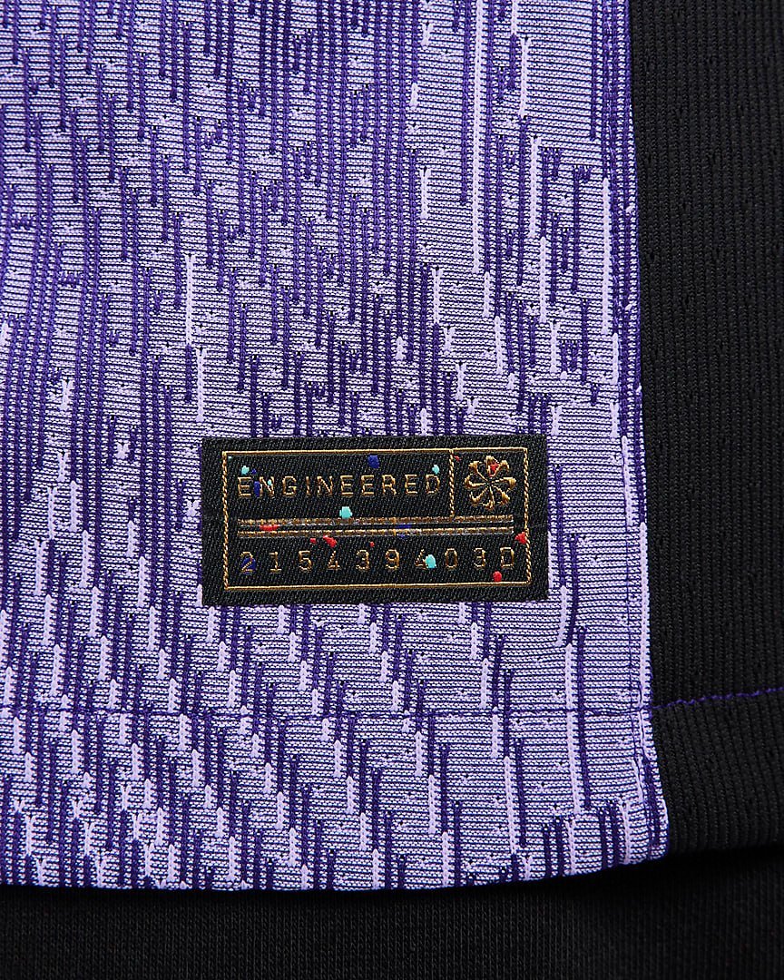 rn-image_picker_lib_temp_fbf162d4-6989-4f18-b32b-e8b98e2b1b23 | UAE SPORT STORE Close-up of purple patterned fabric with a small black tag reading ENGINEERED and a row of numbers nearby.