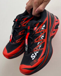 rn-image_picker_lib_temp_fcb8eb45-0874-4b3d-9ab6-42898291842b | UAE SPORT STORE Pair of black and red running shoes with bold diagonal red graphics, held by hand.