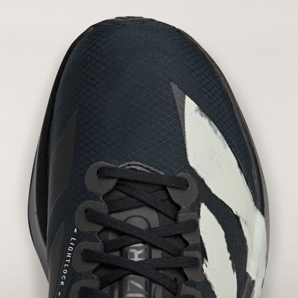 Close-up of a dark athletic sneaker showing laces, textured upper, and a white graphic on a light background