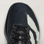 Close-up of a dark athletic sneaker showing laces, textured upper, and a white graphic on a light background