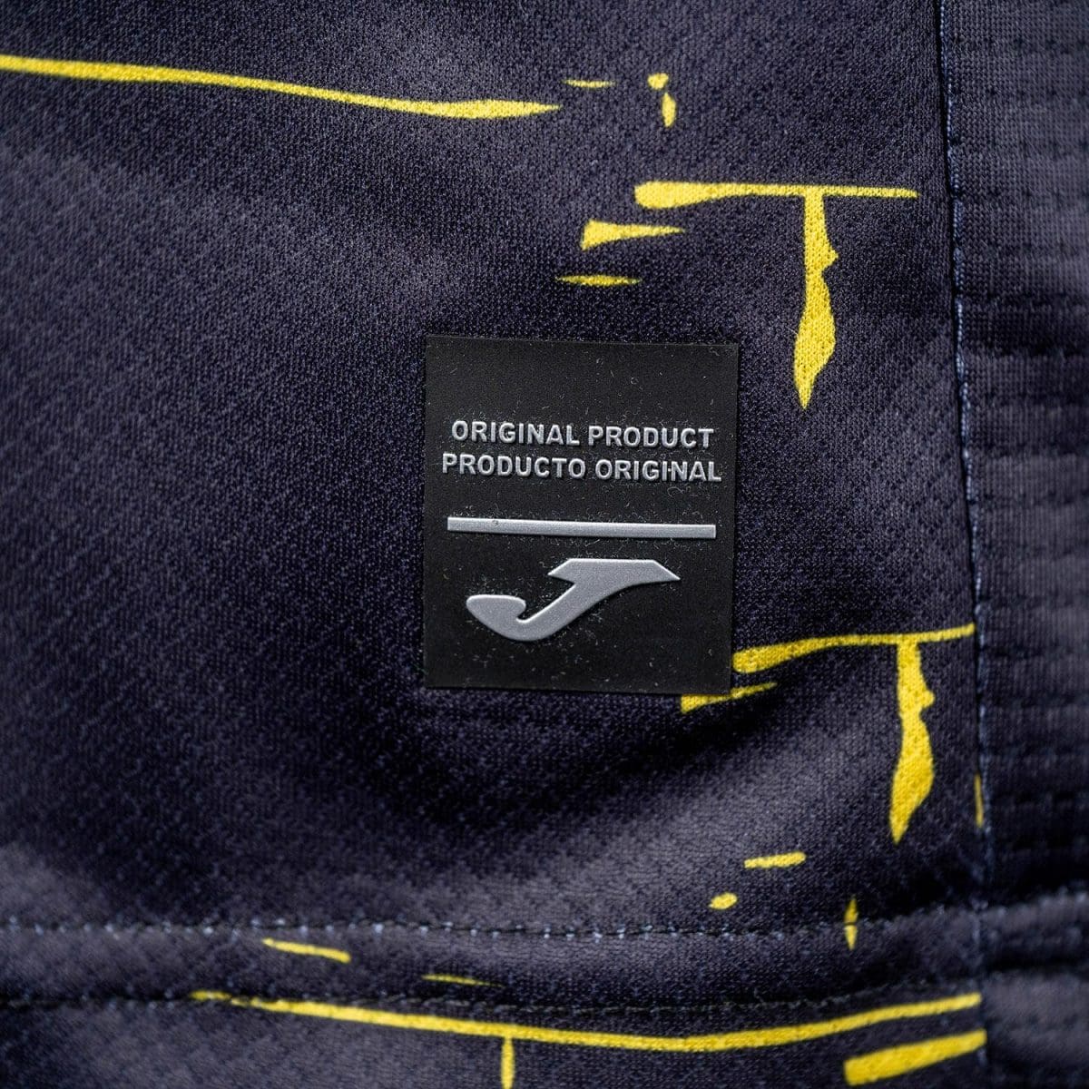 Brand tag on dark fabric: reads 'Original Product / Producto Original' with a silver line and a stylized silver J logo.