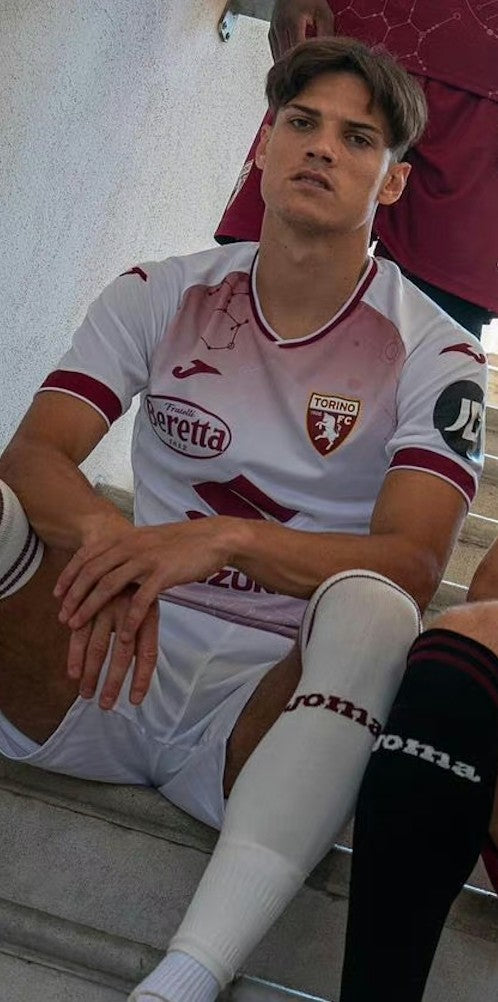ryZsx83USz0kdH2 | UAE SPORT STORE Young male soccer player in a white Torino FC jersey sits on concrete steps, looking at the camera with arms resting on his knees.
