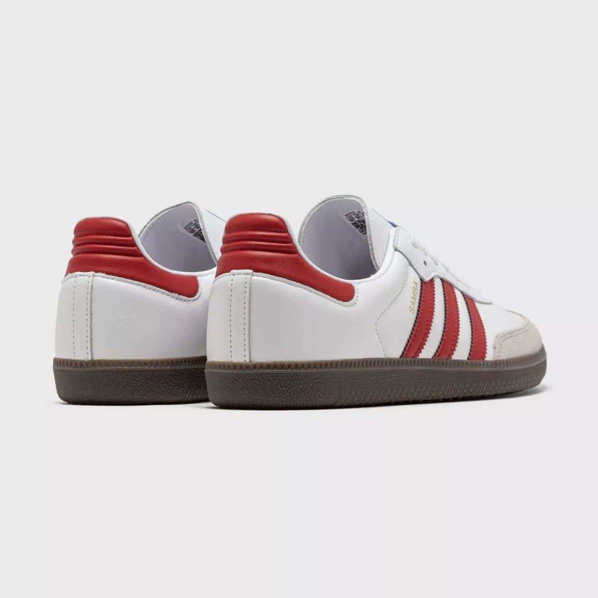 White sneakers with red stripes and a dark sole, viewed from the back-left side of the pair, against a light background.