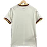 White football jersey hanging on a wooden hanger with burgundy and gold trim on the sleeves and España text at the neck area