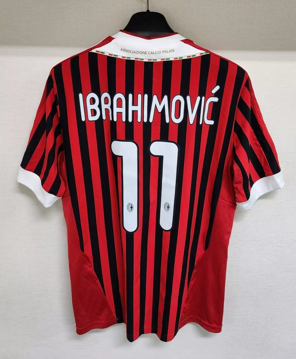 AC Milan home jersey back with Ibrahimović 11 on red and black vertical stripes, hanging on a hanger
