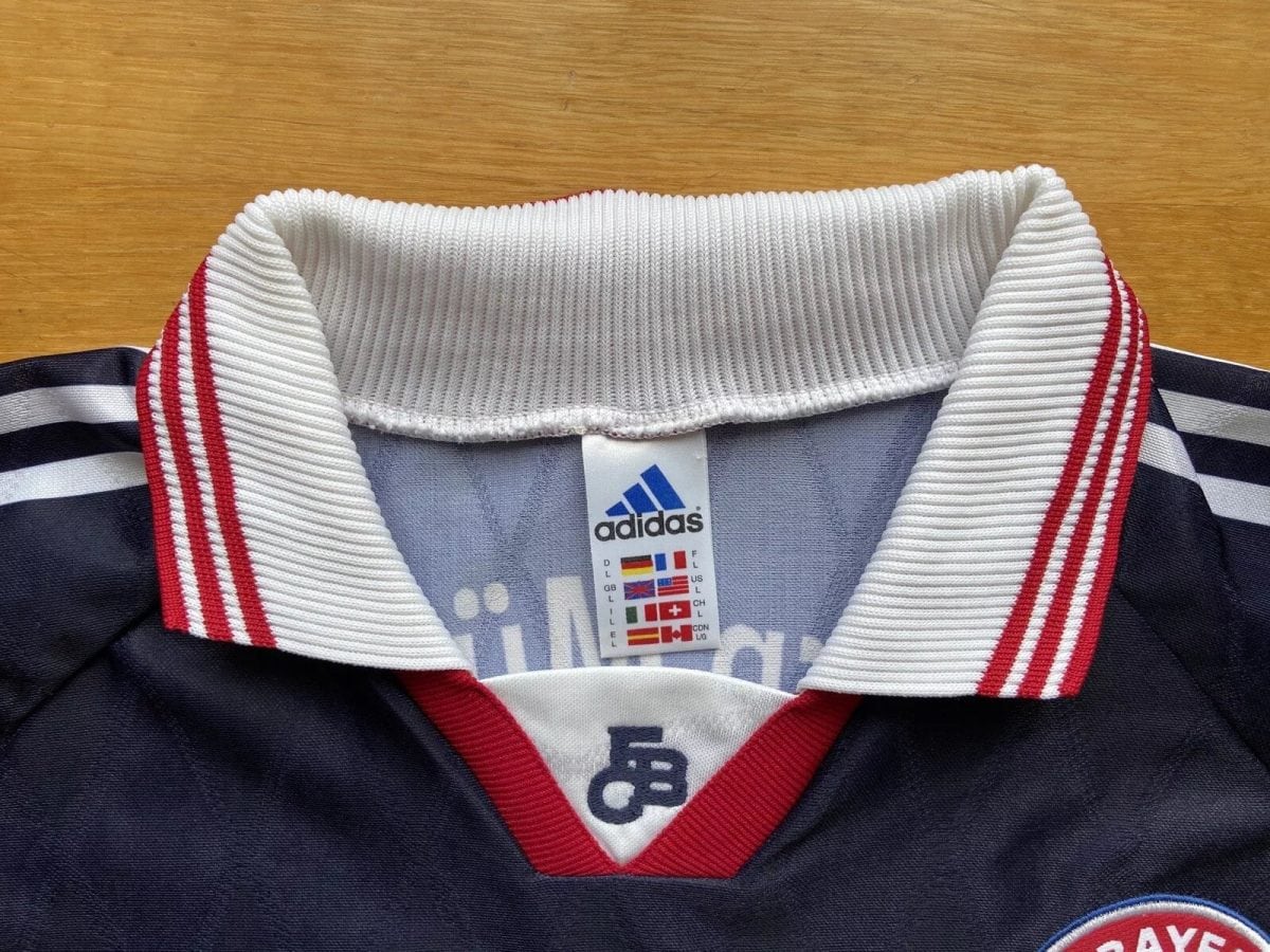 Close-up of a navy polo shirt collar with a white ribbed edge and red stripes, Adidas logo tag visible inside the collar.