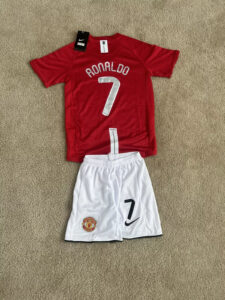 s-l1600_2_828cdce6-0d14-4f1c-ba00-f738b64f2beb | UAE SPORT STORE Red Manchester United kid's soccer jersey with 'RONALDO' and number 7 on the back, paired with white shorts displaying the club crest and a large 7.